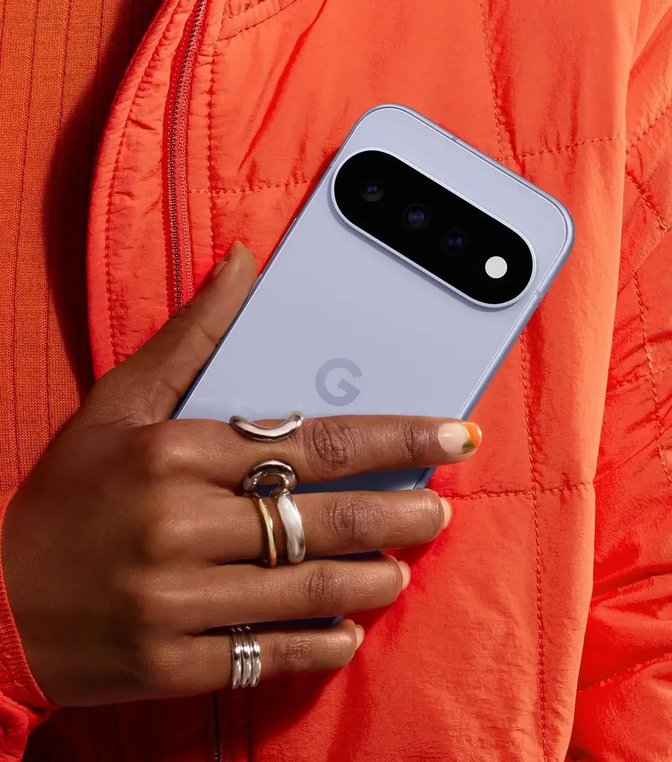 Google Pixel 11 — Frost renkli Google Pixel 11'in arka yüzü: üç kameralı kamera adası. Üretici mağaza sayfasındaki fotoğrafta telefon elde tutuluyor.